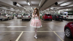 Det är lätt att skapa kontraster med Lolitastilen. En kvinna klädd i så kallade Lolitakläder - en fluffig vit och rosa klänning med spetsar på. Hon har vita högklackade skor och blommor i håret. Hon står i en parkeringsgrotta.