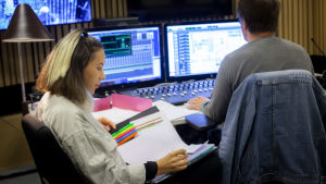 Isabel Cruz Liljegren har regisserat ett hörspel om kvinnlig vänskap i samarbete med Blaue Frau, den kommer att ha premiär i december på Yle Vega. Klipparen vi ser ryggen av är Nico Ingman. Isabel Cruz Liljegren sitter i studion och läser i sina papper.