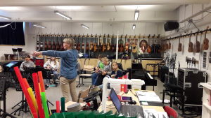 Spel och sång i samspel. Musiklärare Marina Lindholm står mitt i klassen och instruerar elever som sitter i ring med musikinstrument i famnen.
