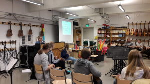 Ukulelen är pop. Elever sitter i ring och spelar ukulele medan musiklärare Marina Lindholm ackompanjerar vid pianot.
