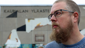 Kuvassa Tuomas Kyrö seisoo Kaurialan yläasteen edessä. Koulun nimi näkyy seinässä.