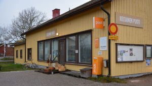Ett av husen i centrum. Ett gulmålat trähus i Gustavs med stora skyltfönster och postens logo utanpå.