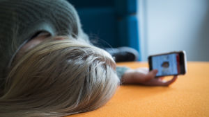 Nätmobbning är ett stort problem i synnerhet bland unga. En flicka ligger på en soffa och granskar sin telefon.