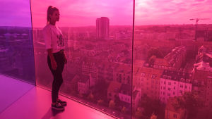 Vogue Williams: Sokerideittailu. Nainen seisoo pilvenpiirtäjässä huoneessa, jonka seinät ovat lasia. Värit puna-violetti.