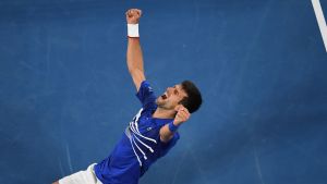 Novak Djokovic jublar efter sin 15:e Grand Slam-seger. Tennisstjärnan Novak Djokovic jublar på knä med händerna i luften.