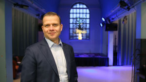 Samlingspartiets partiordförande Petteri Orpo. Petteri Orpo taustalla violeteilla spoteilla valaistu näyttämösali.