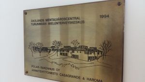 En mässingsskylt med en bild av och text om att Åbolands mentalvårdscentral är byggd 1994.