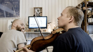Pekka Kuusisto soittaa viulua, Samuli Koskinen katsoo Kuusistoa taustallaan aukioleva tietokone.