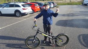Sisu Kymäläinen får 300 euro av Sjundeå kommun. Pojke står på en parkeringsplats med en pokal i handen vid sin cykel.
