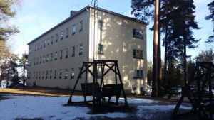 Trägungor på en snöig gräsmatta framför en ljusgul stenbyggnad i tre våningar, Esperi Hoitokoti Rehabia.
