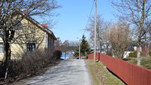 Barnen hoppas att fler klasskompisar skulle flytta ut. En väg och ett gult gammalt hus, ett rött staket. Man ser havet vid vägens slut.
