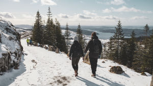 Elin och Andreas vandrar ner för Fløyfjellet längs med en bred stig, i bakgrunden syns ett vackert fjordlandskap.