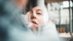 F (Fanni Sjöholm) katsoo kameraan kädessä olevan peilinpalasen kautta, josta näkyy hänen kasvonsa.