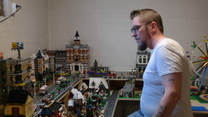 Peter Palander i en vit tshirt. Han står framför en detaljrik legostad i flera våningar.