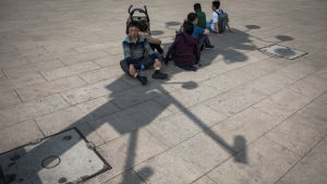 Övervakningskameror fäller en skugga över en grupp kinesiska turister som sitter vid Himmelska fridens torg i Peking. Kinesiska turister vilar ut vid Himmelska fridens torg i skuggan av ett torn av övervakningskameror.