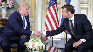 President Trump och president Macron träffades. Trump skakar hand med Macron framför en amerikansk flagga.