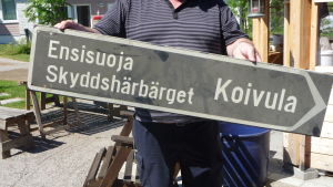 Arkivbild. En man håller i en skylt som pekar till höger. På skylten står Skyddshärbärget Koivula.