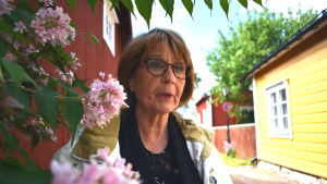 Mona Blomqvist ville lära känna hemstaden bättre. Kvinna med mörkt hår och i vit jacka står vid en buske vid en grusväg.