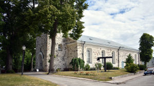 Den gamla kyrkan brann 1821. En vit stenkyrka med gräsmatta och grusväg utanför.