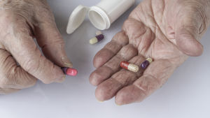 Hemvårdarna ser bland annat till att klienterna tar sina mediciner. En äldre person håller i tabletter med en läkemedelsburk framför sig.