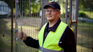 Micke i en gul ordningsmansväst framför gallerporten till backstageområdet. Ena handen vilar på handtaget.