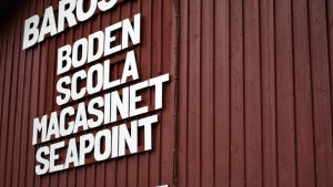 Företaget Villa Barö driver restaurangen Scola i Barösunds hamn. Bokstäver på en träfasad.