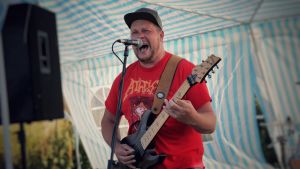 Gitarristen och solisten Han Ted från Napalm Ted fick publiken att röra sig. En man i röd skjorta spelar gitarr och skriker i en mikrofon