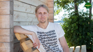 Jaakko Blomberg istuu puisella penkillä saunarakennuksen vierustalla.