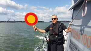 Under detta år har man längs hela västkusten granskat mer än 5 000 båtar. De flesta anmärkningarna har gällt flytvästar och brandsläckare. Löjtnant Mika Stormblad från Nagu sjöbevakningsstation håller upp en rödgul stoppskylt i samband med sjöbevakningens övervakning till sjöss.