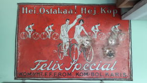 Sture Walls har den här sällsynta skylten på sin vägg i cykelaffären. En röd gammal skylt i metall som visar ett par som cyklar. På skylten står det: Hej! Köp Felix Special.
