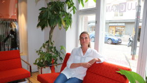 Ann-Jolin Grüne är utvecklingschef på Luckan Integration i Helsingfors. En kvinna sitter på en soffa. Hon är klädd i skjorta och jeans och bakom henne finns ett fönster som vetter mot en gata. På gatan står en bil och en motorcykel.