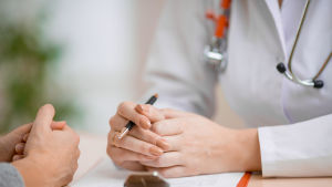 Närbild av händerna av en läkare och dennes patient. De sitter mot varandra och samtalar.