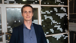 Tommi Lahtinen på Silverskin. Tommi Lahtinen står i kavaj och skjorta framför en vägg som där dekorerad med ettor och nollor.