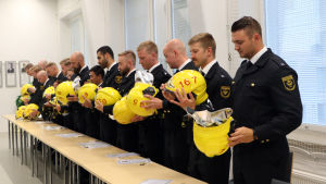 Det nyblivna räddningsmanskapet drar på dig sina hjälmar. Brandmännen lägger på sina hjälmar.