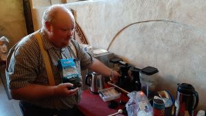 Magnus Taxell kokar kaffet denna söndag. Magnus Taxell, en man med rödaktig mustasch och skägg, rutig skjorta och gyllene hängslen, kokar kaffe inför kyrkkaffet i Åbo Domkyrkas sakristia.