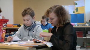 Oskar Stenfors får hjälp av Inga Sahlberg. Förskolan till och med fjärdeklassarna är i en grupp. elev och lärare vid en pulpet och tittar i en bok