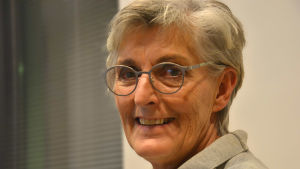 Margita Vainio. Margita Vainio, en glad dam med grått hår och glasögon med silverfärgade skalmar.