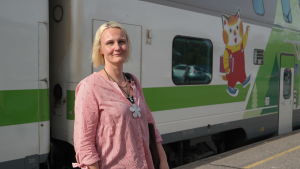 Linnea Henriksson står bredvid ett tåg med en bild av en katt som visar att här finns barnvagn
