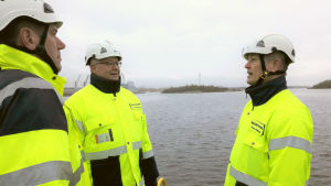 Jaakko Aerila från Raumo stad samt Hannu Asumalahti och Timo Metsäkallas från Raumo hamn hoppas att vägbanken till Iso Järviluoto snart kunde byggas. Tre män i gula västar och vita skyddshjälmar diskuterar i Raumo hamn.