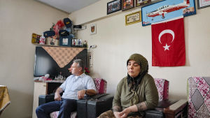 Nainen ja mies istuvat kodissa, seinällä Turkin lippu.