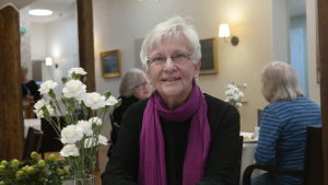 Ingalill Karlsson tjuvstartade i Åbo Svenska Pensionärsklubb Ingalill Karlsson sitter vid ett bord bredvid en vas med vita nejlikor. I bakgrunden två andra damer.