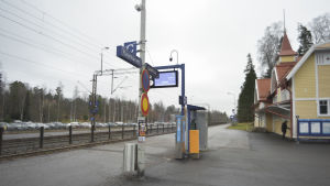 En del av misshandeln skedde på tågspåret vid Grankulla tågstation. En perrong på en tågstation. Det är en mulen höstdag. En man står vid en byggnad på stationen.