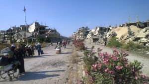 Ihmisiä kantamuksineen raunioituneessa Homsin kaupungissa Syyriassa