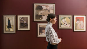 På Ateneum. Helene (Laura Birn) framför några av sina verk. Helene framför sina tavlor som hänger på en röd vägg.
