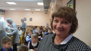 Rektorn Nina Kovaljova tycker skollunchen är viktig. En leende kvinna framför barn som äter skolmat.