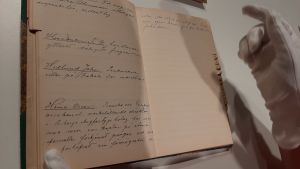 Kunderna finns prydligt dokumenterade i anteckningsboken. En hand med vit handske bläddrar försiktigt i en gammal anteckningsbok.