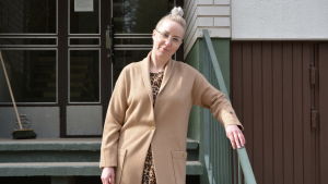 Heidi Svartsjö utanför det hus där hon bodde som barn. Kvinna i beige kappa framför höghus.