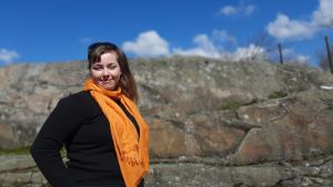 Jessica Österberg tror att många studerande kan tvingas tänka om gällande sommarplaner i år. Ung kvinna med brunt hår och orange halsduk står vid stenig klippa