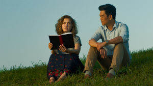 Haley Lu Richardson ja John Cho elokuvassa Columbus. Nuori amerikkalainen nainen ja korealainen mies istuvat nurmikolla, naisella on kirja kädessään.