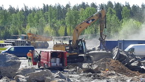 Företagare gillar att Ingåport syns från stamväg 51. Synlighet är viktigt, säger de. Män och arbetsmaskiner bland stenar som sprängts på Ingåport.